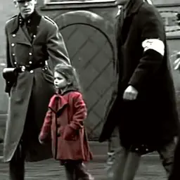 Mała dziewczynka w czerwonym płaszczyku idzie obok żołnierzy.