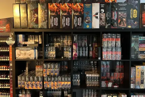 Półki pełne pudełek z grami i figurkami, w tym wiele z serii Warhammer. Widać tu zapowiedź przygód Gotreka i Felixa, a także inne tytuły.